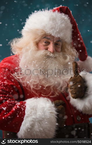 Santa Claus standing outdoors at snowfall at north pole and showing thumb up