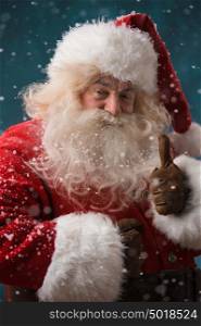 Santa Claus standing outdoors at snowfall at north pole and showing thumb up