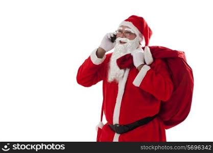 Santa Claus talking on mobile phone while carrying sack over white background
