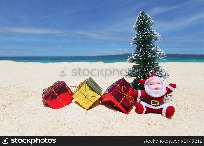 Santa Claus with fir tree and gifts on sand at tropical ocean beach, Christmas and New Year winter vacation concept