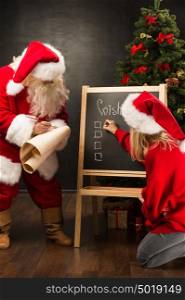 Santa Claus with his helper standing near chalkboard with wishlist sign and blank copy space for checkboxes and your text.