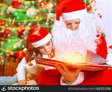 Santa Claus with little granddaughter opening magic book and saw glowing lights, spending Christmas eve near beautiful decorated tree