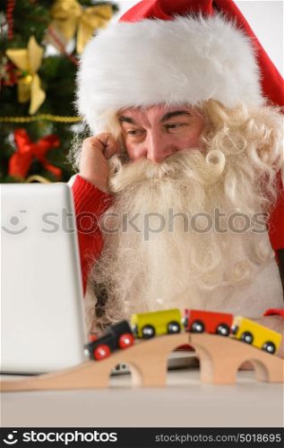 Santa Claus with real beard using laptop, Christmas tree in background