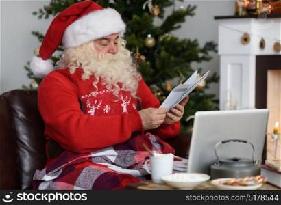 Santa Claus Working near Christmas Tree at Home. Reading childrens letters