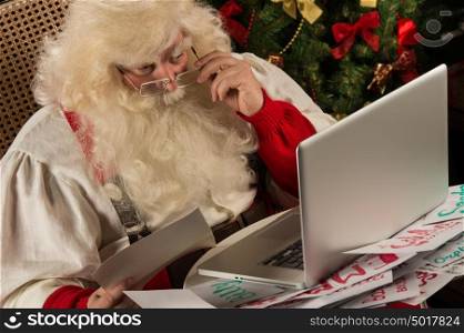 Santa Claus working on computer reading emails and paper letters from children from all over the world