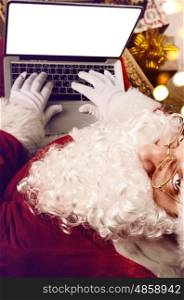 Santa Claus working with modern laptop on his lap, view from above