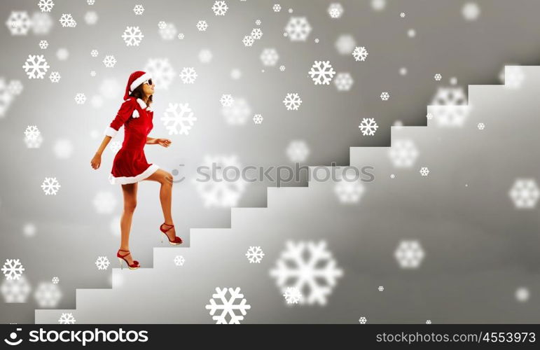 Santa girl. Attractive young woman in Santa suit walking on ladder