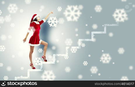 Santa girl. Attractive young woman in Santa suit walking on ladder