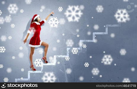 Santa girl. Attractive young woman in Santa suit walking on ladder