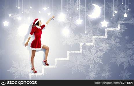 Santa girl. Attractive young woman in Santa suit walking on ladder