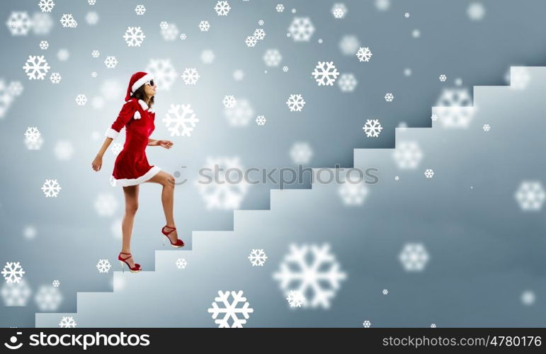 Santa girl. Attractive young woman in Santa suit walking on ladder