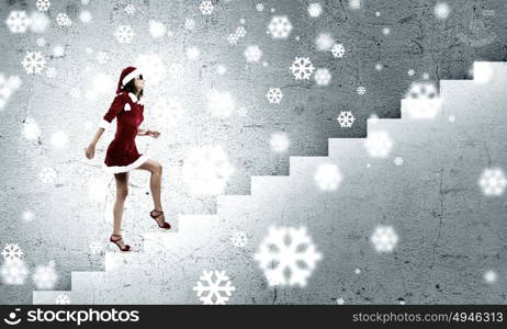 Santa girl. Attractive young woman in Santa suit walking on ladder