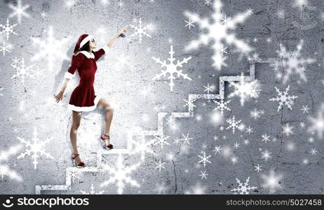 Santa girl. Attractive young woman in Santa suit walking on ladder