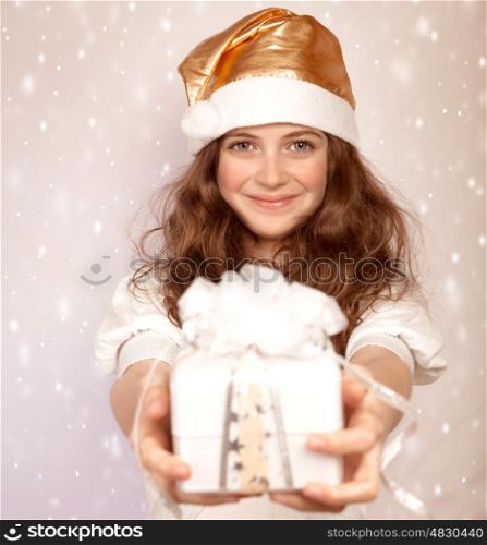 Santa girl offers gift box, cute teenager wearing shiny hat isolated on pink snowing background, Christmastime surprise