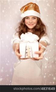 Santa girl offers gift box, cute teenager wearing shiny hat isolated on pink snowing background, Christmastime surprise