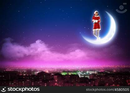 Santa girl on the moon. Santa Claus girl on the moon above a city at night