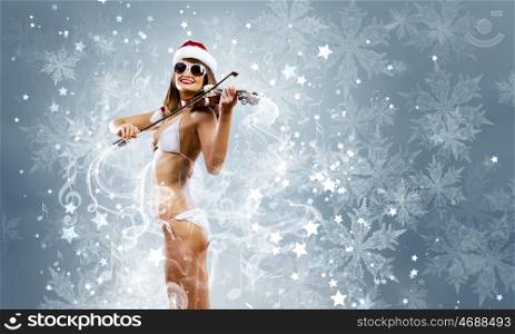 Santa girl. Young woman in swimming suit and santa hat playing violin