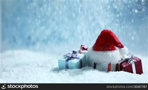 Santa hat and small decorative gifts under falling snow, Christmas time New Year background