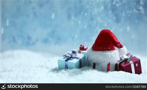 Santa hat and small decorative gifts under falling snow, Christmas time New Year background