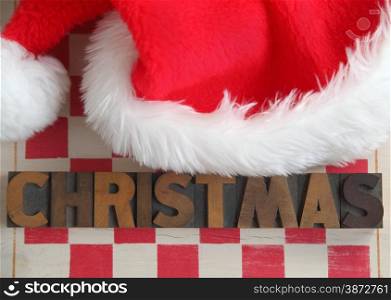 Santa hat on stenciled checkerboard with the word &rsquo;Christmas&rsquo; in old wood type