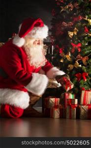 Santa putting gifts under Christmas tree in dark room