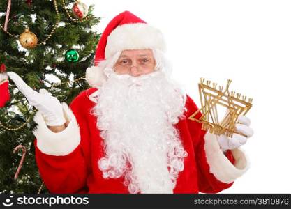 Santa standing in front of a Christmas tree holding a menorah.