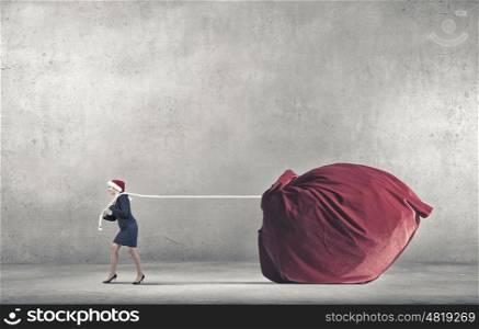 Santa woman deliver gifts. Woman in Santa hat pulling huge red gifts bag