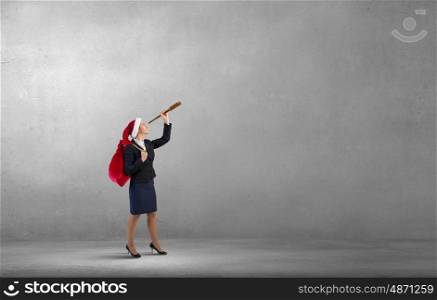 Santa woman in search. Businesswoman in Santa hat in concrete room looking in spyglass