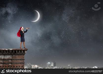 Santa woman in search. Businesswoman in Santa hat on building top looking in spyglass