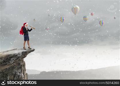 Santa woman in search. Businesswoman in Santa hat on rock top looking in spyglass