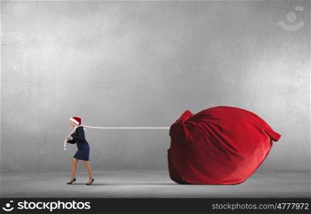 Santa woman with huge sack. Woman in Santa hat pulling huge red gifts sack