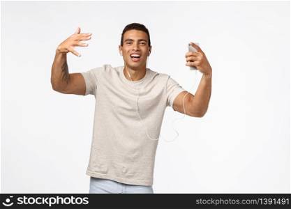 Sassy and arrogant cool hispanic man in t-shirt, shaking hands and dancing, singing along favourite songs, wear wired earphones, hold smartphone, enjoy nice music playlist, white background.. Sassy and arrogant cool hispanic man in t-shirt, shaking hands and dancing, singing along favourite songs, wear wired earphones, hold smartphone, enjoy nice music playlist, white background