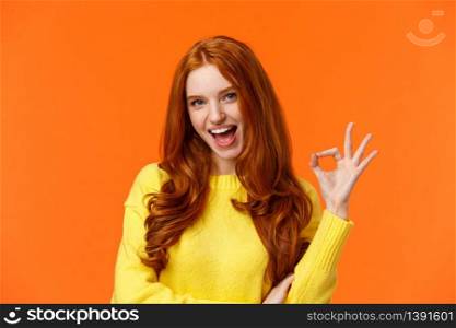 Sassy and daring cool redhead girl with curls, showing okay excellent gesture and smiling excited, assure party be awesome, give permission, say yes, confirm or recommend something, orange background.. Sassy and daring cool redhead girl with curls, showing okay excellent gesture and smiling excited, assure party be awesome, give permission, say yes, confirm or recommend something, orange background
