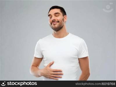 satisfaction and people concept - happy full man touching his tummy over gray background. happy full man touching tummy over gray background