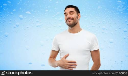 satisfaction, healthy eating and people concept - happy full man touching his tummy over blue wet background