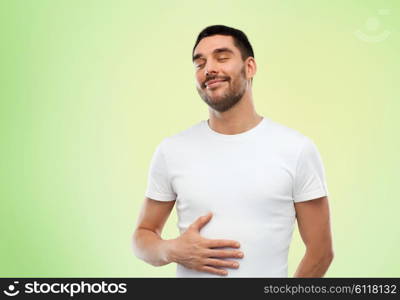 satisfaction, healthy eating and people concept - happy full man touching his tummy over green background