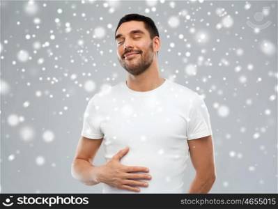 satisfaction, winter, christmas and people concept - happy full man touching his tummy over snow on gray background