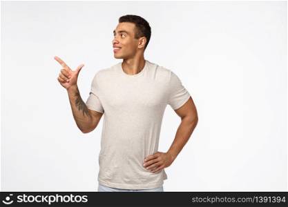 Satisfied and proud, smiling happy hispanic man with short haircut, tattoo, wear casual t-shirt, looking and pointing upper left corner with pleased expression, reading sign, recommend product.. Satisfied and proud, smiling happy hispanic man with short haircut, tattoo, wear casual t-shirt, looking and pointing upper left corner with pleased expression, reading sign, recommend product