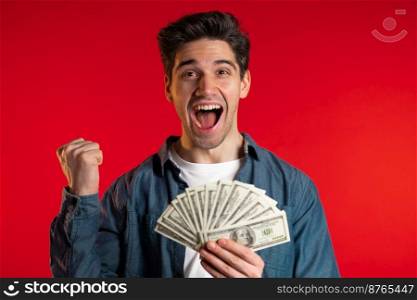 Satisfied happy excited man showing money - U.S. currency dollars banknotes on red wall. Symbol of success, gain, victory. Satisfied happy excited man showing money - U.S. currency dollars banknotes on red wall. Symbol of success, gain, victory.