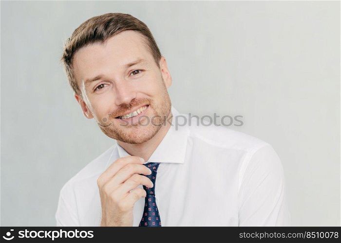 Satisfied male worker with positive expression, has broad smile, rejoices sucessful agreement with partner, wears elegant clothes, isolated over white studio wall. People, positive emotions concept