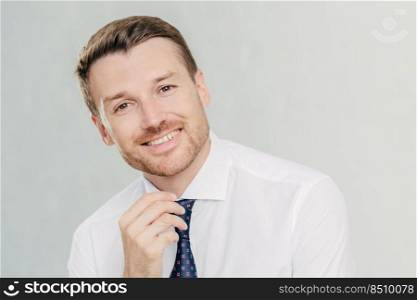 Satisfied male worker with positive expression, has broad smile, rejoices sucessful agreement with partner, wears elegant clothes, isolated over white studio wall. People, positive emotions concept