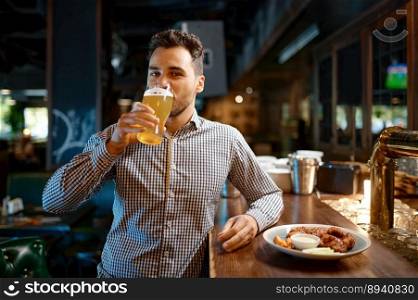 Satisfied man drinking cold fresh craft delicious beer while rest at sports bar. Young man standing at counter desk looking at camera while tasting foamy beverage. Satisfied man drinking cold fresh craft beer while rest at sports bar