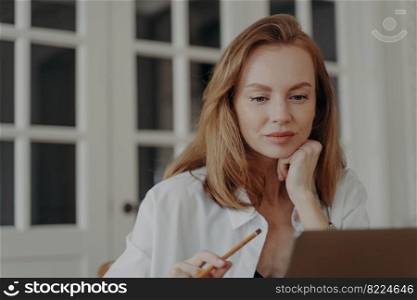 Satisfied mid adult businesswoman is working at laptop from her apartment. Attractive elegant european lady is freelancer, entrepreneur or accountant. Woman has online chat. Remote work concept.. Satisfied mid adult businesswoman is working at laptop from her apartment. Remote work concept.