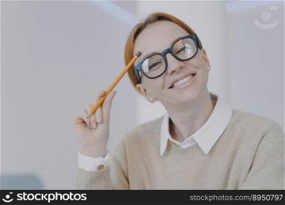 Satisfied pretty girl is studying. Happy student holding pencil, reading on computer and taking notes. Young creative european businesswoman in glasses. Remote study or distance work concept.. Satisfied girl is studying, reading and taking notes. Remote study or distance work concept.