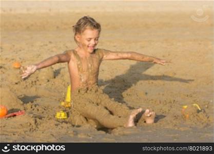 Satisfied six year old girl to roll yourself wet sand on the beach