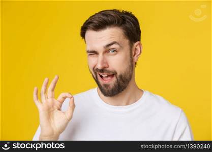 Satisfied young man showing okay sign isolated on yellow background. Satisfied young man showing okay sign isolated on yellow background.