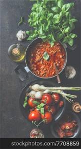 Sauce bolognese in black cooking pot on dark kitchen table background with ingredients. Top view