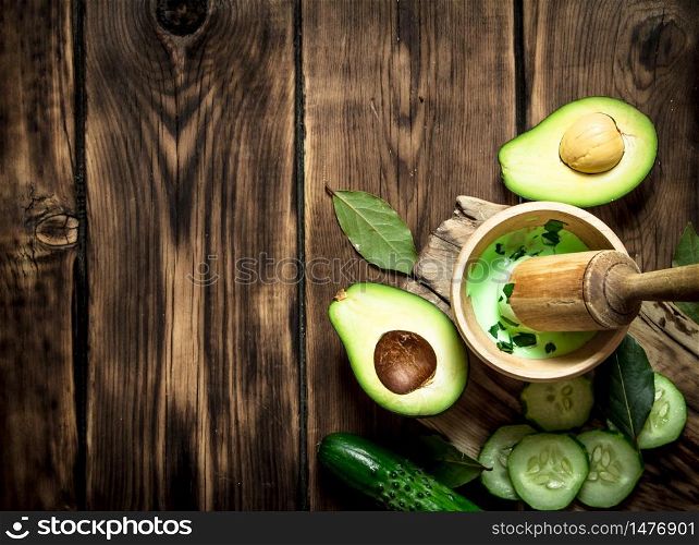 Sauce in a mortar with pestle, avocado and cucumber. On wooden background.. Sauce in a mortar with pestle, avocado and cucumber.