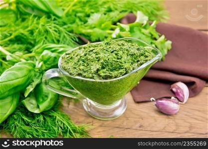 Sauce of dill, parsley, basil, cilantro, other spicy herbs, garlic and vegetable oil in a glass gravy boat, a napkin on wooden board background