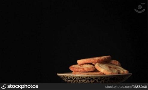 Saucer with cookies on black background.